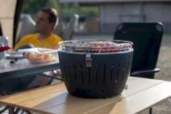 LotusGrill XL Hybrid Houtskoolbarbecue - Rood 20 LotusGrill XL Hybrid Houtskoolbarbecue - Rood -Camping Verkoopwinkel lotusgrill in gebruik met toppy shirtje 2